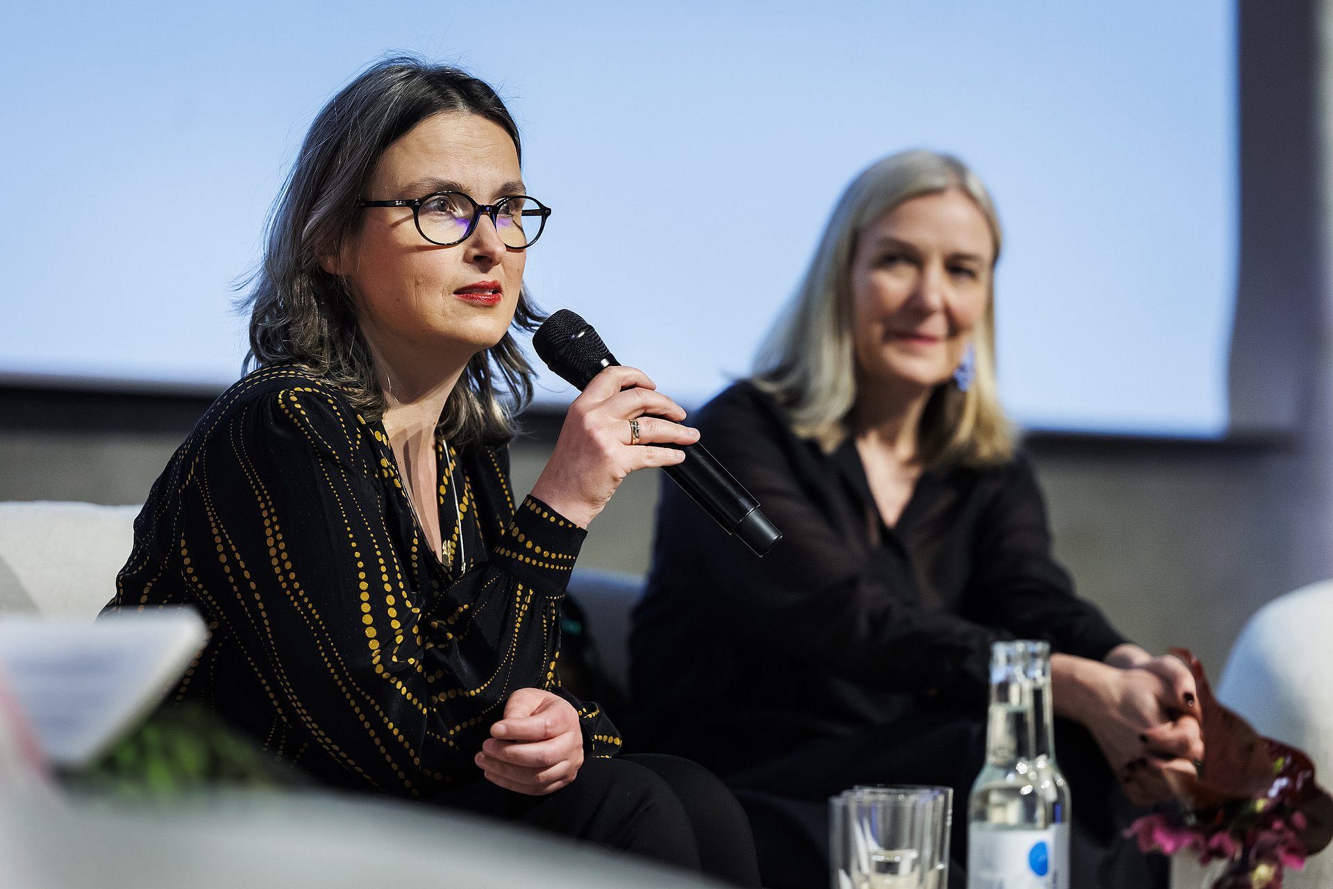 Magdalena Saryusz-Wolska spricht auf einem Podium in ein Mikrofon; neben ihr sitzt Marion Ackermann und hört zu.