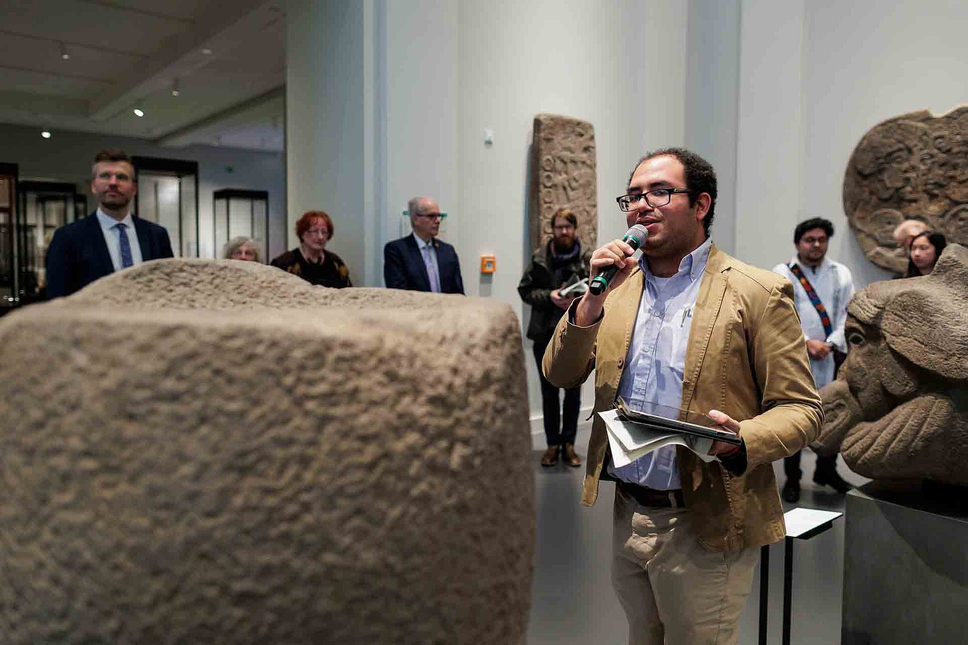 Ein Mann mit Mikrofon erklärt Personen etwas in einem Ausstellungsraum