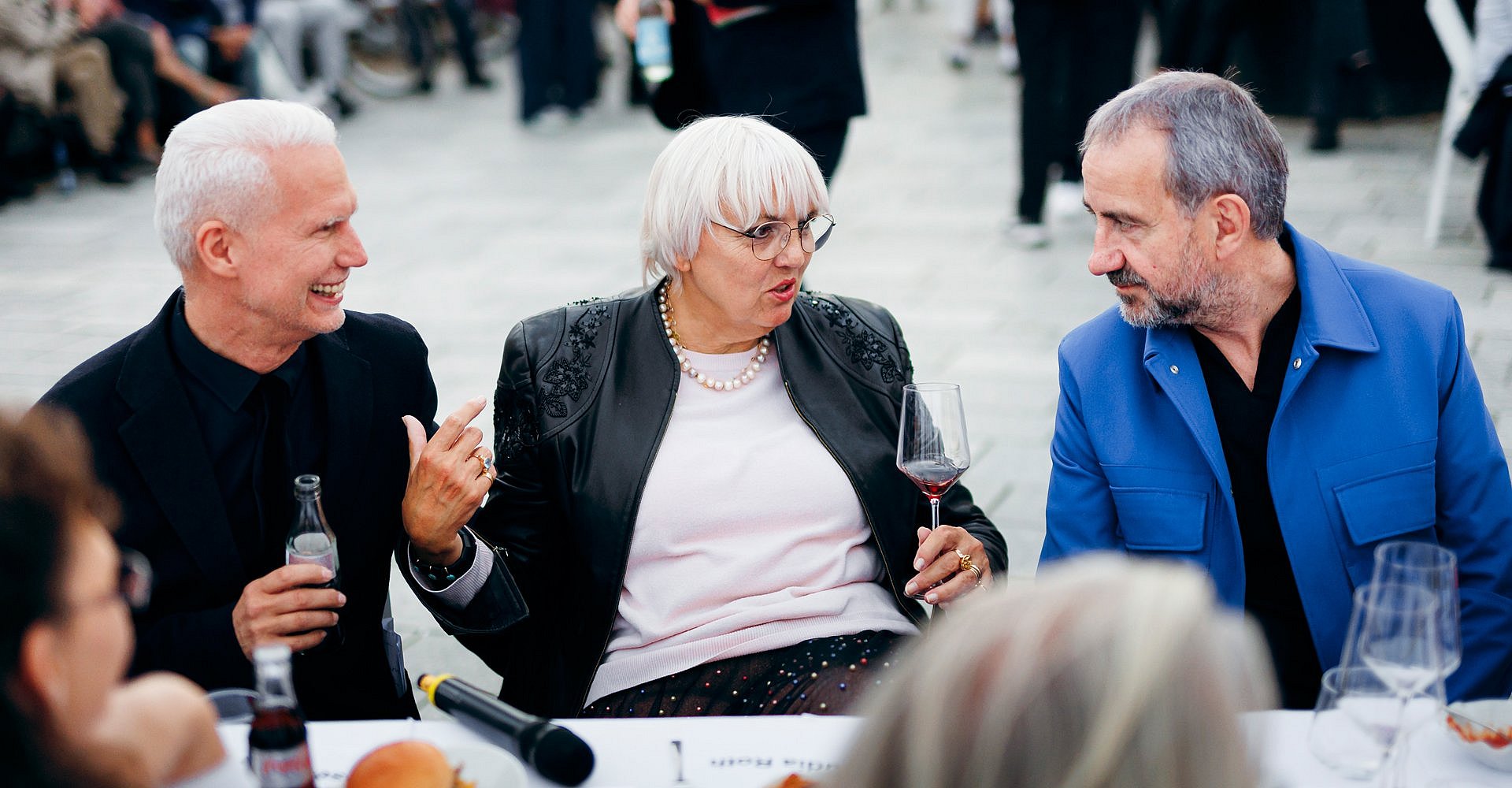 Drei Personen mit Weingläsern an einer Tafel im Freien