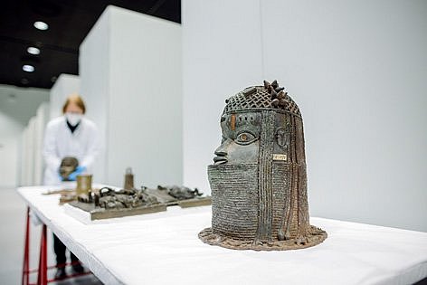 Eine Skulptur steht auf einem weißen Tisch, im Hintergrund eine Frau im Kittel (öffnet Vergrößerung des Bildes)