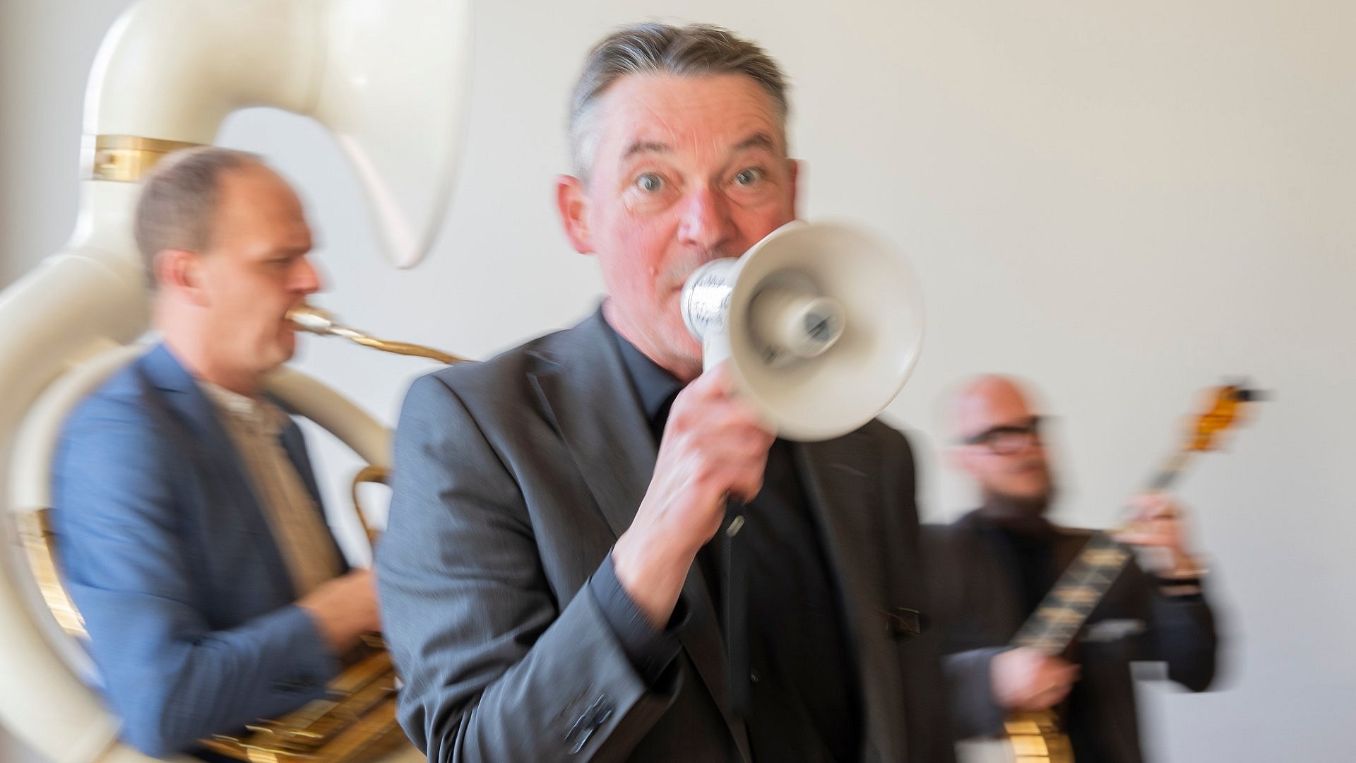 Mann singt in ein Mikrofon, im Hintergrund eine Kapelle mit Bläser und Banjo