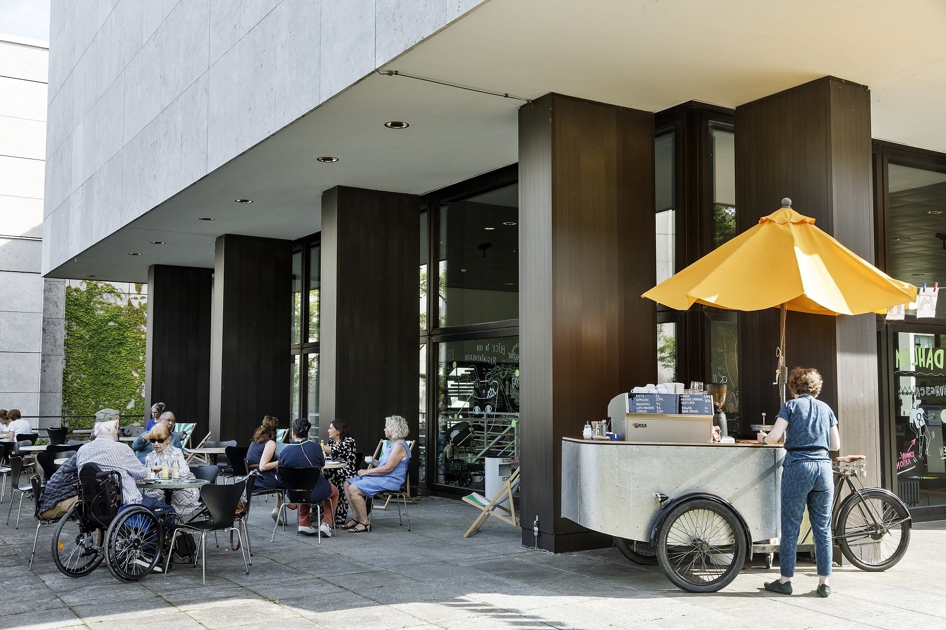 Ein Eiswagen vor einem Gebäude. Menschen sitzen an Tischen