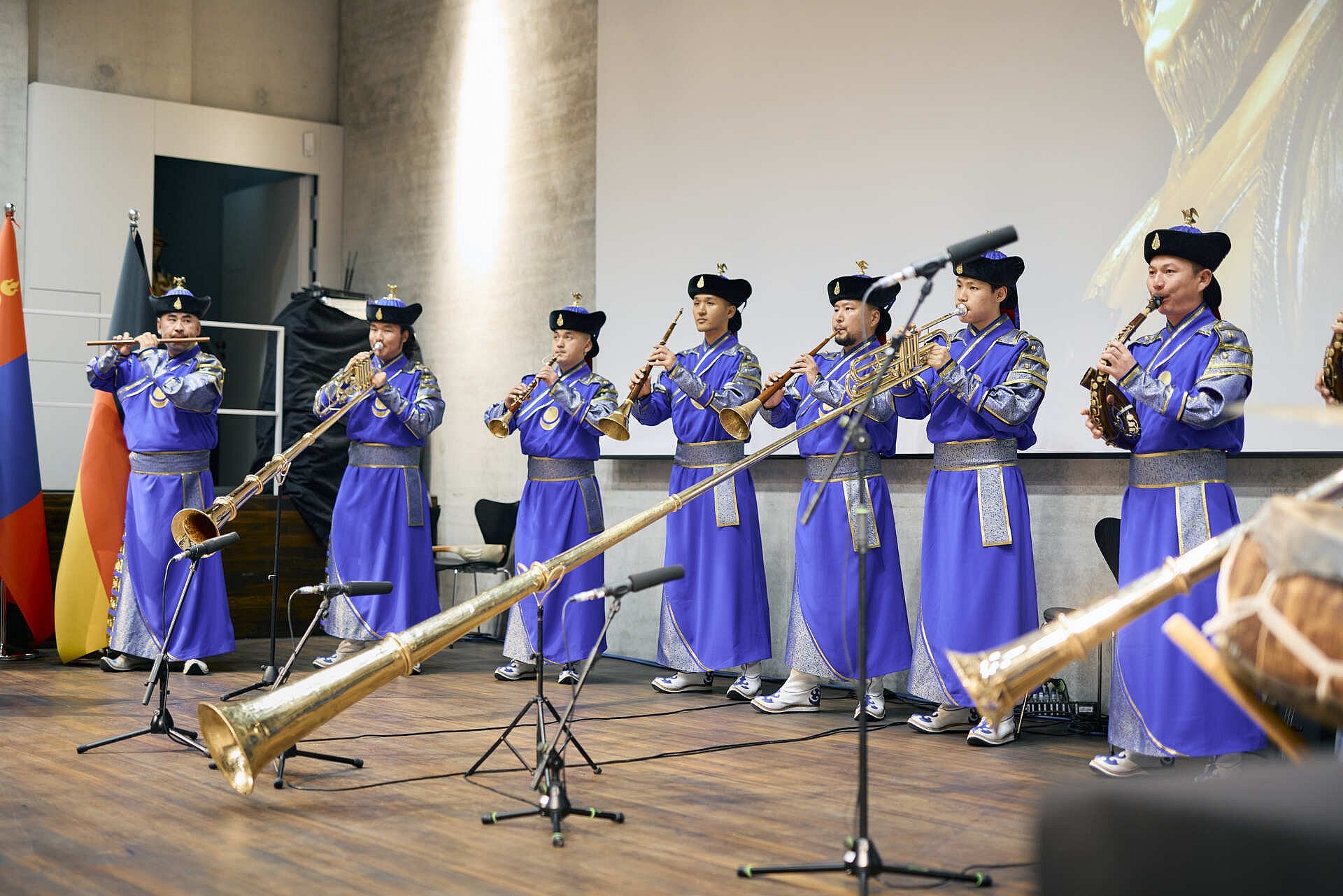 Ein Ensemble in blauen Gewändern und Hüten spielt auf Saiten- und Blasinstrumenten vor mehreren Mikrofonen.