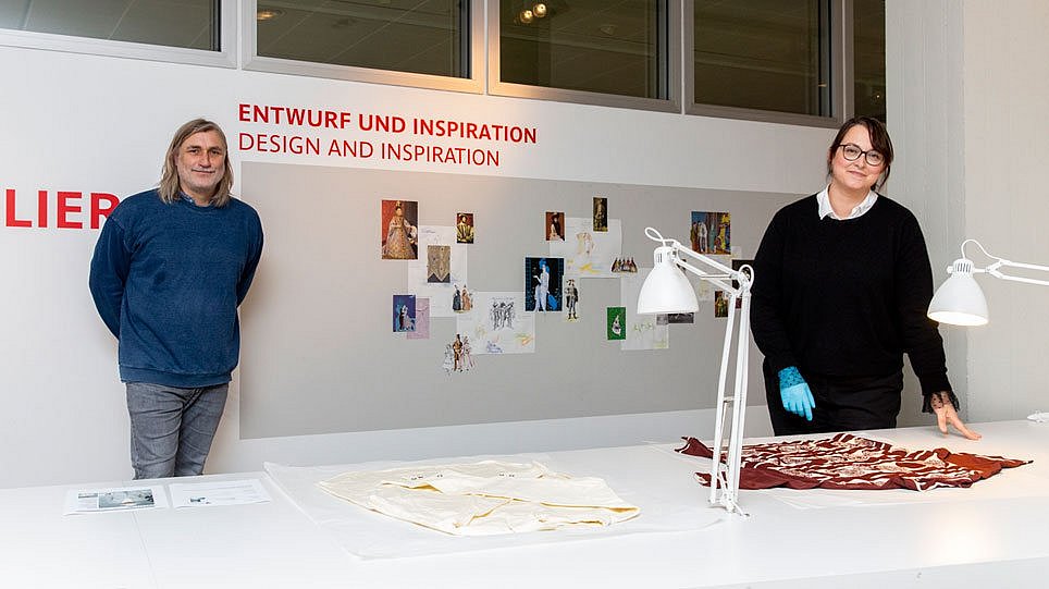 Zwei Personen stehen mit Abstand hinter einem großen Tisch