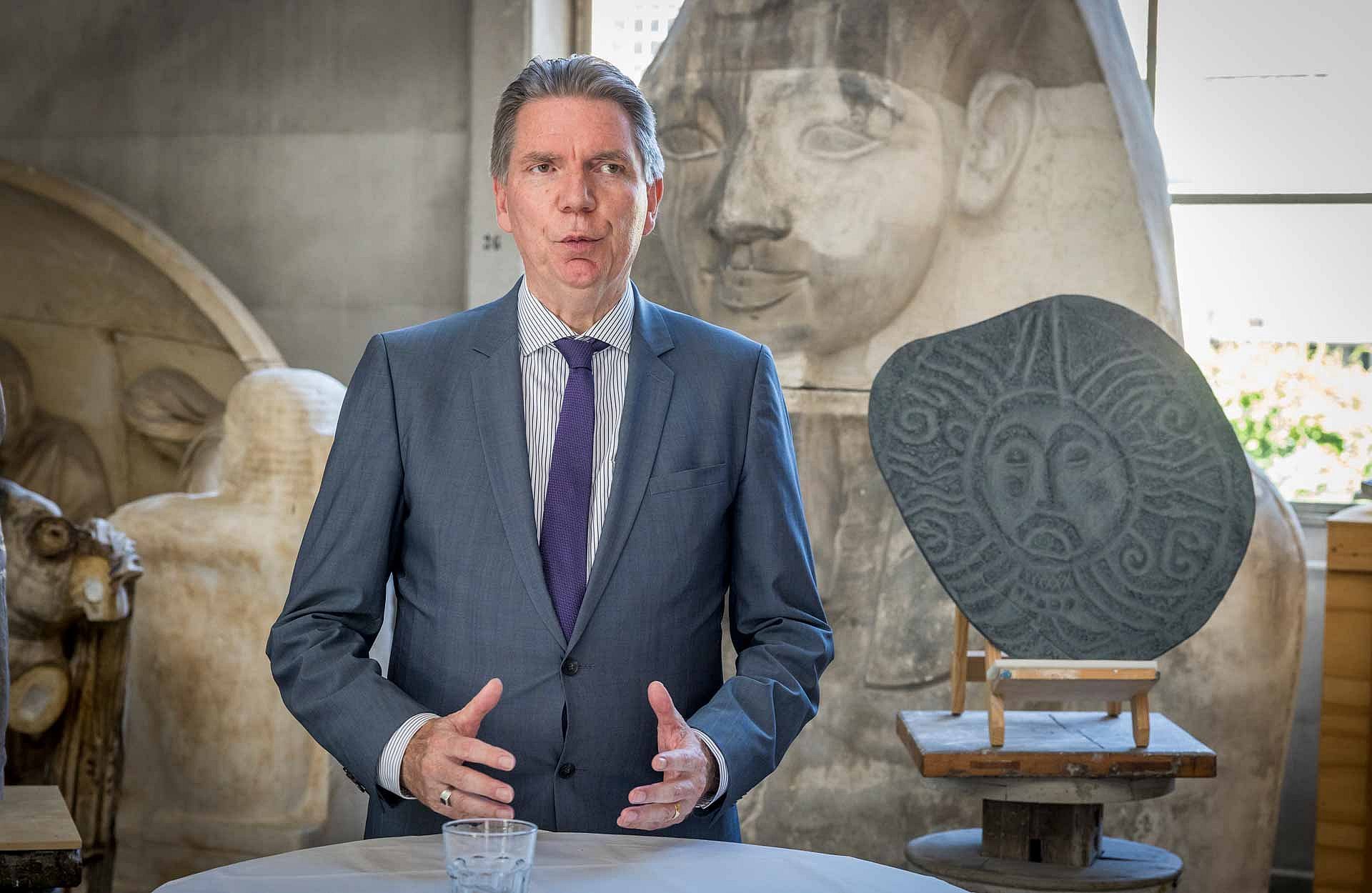 Mann spricht, im Hintergrund Steinobjekte in einer Werkstatt