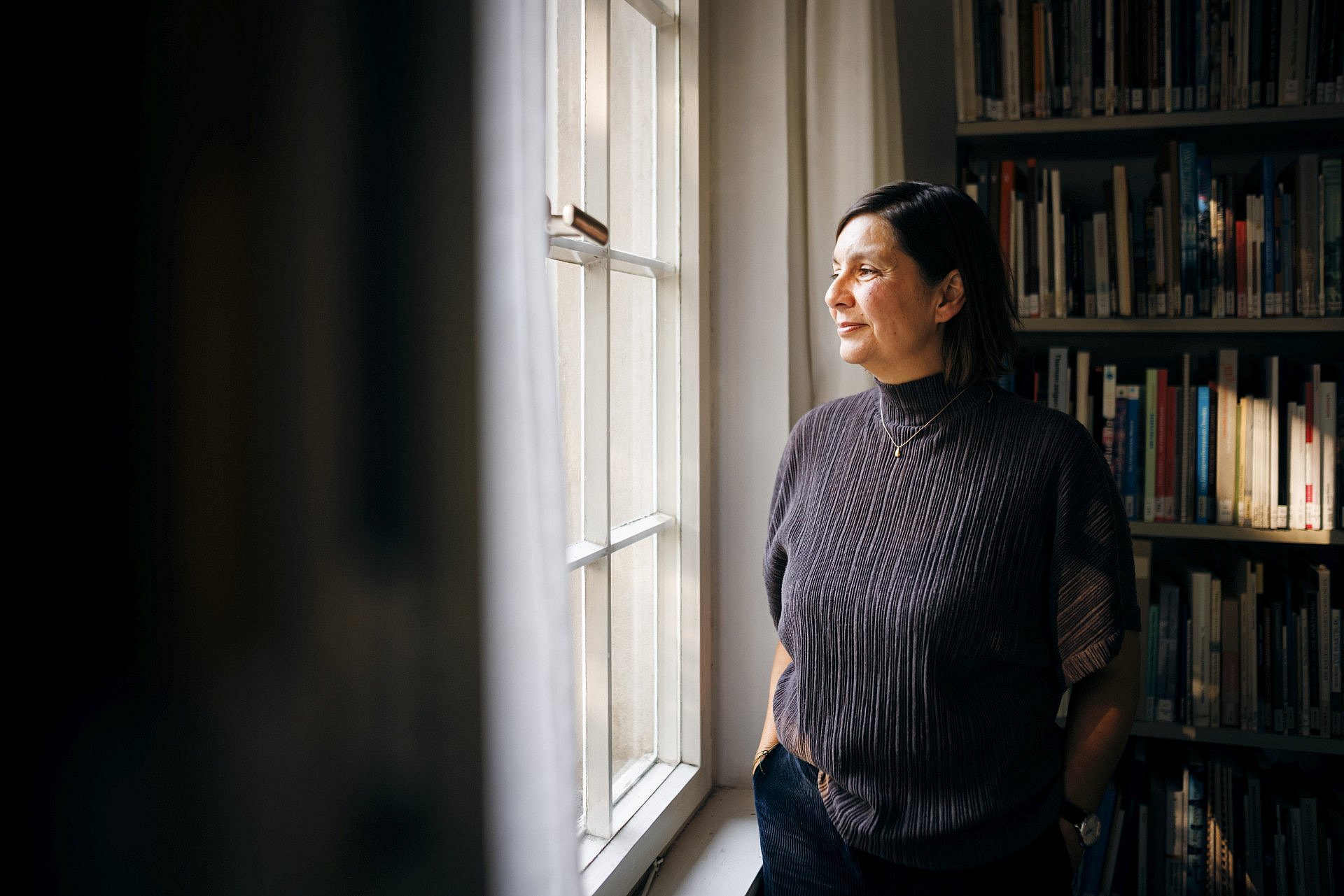 Portrait einer Frau in einem Arbeitszimmer. Sie blickt aus dem Fenster