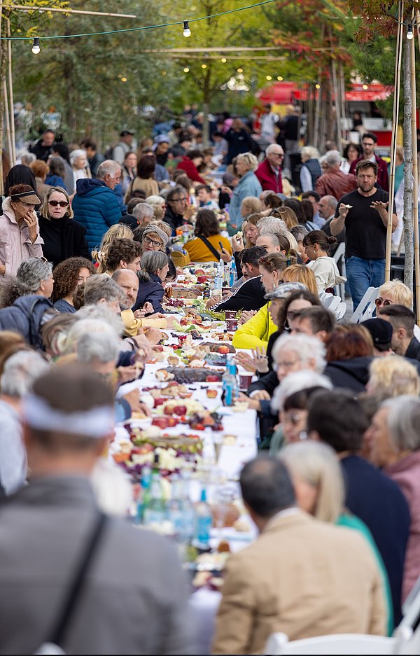 Menschen sitzen im Freien unter Bäumen an einer reichlich gedeckten Tafel