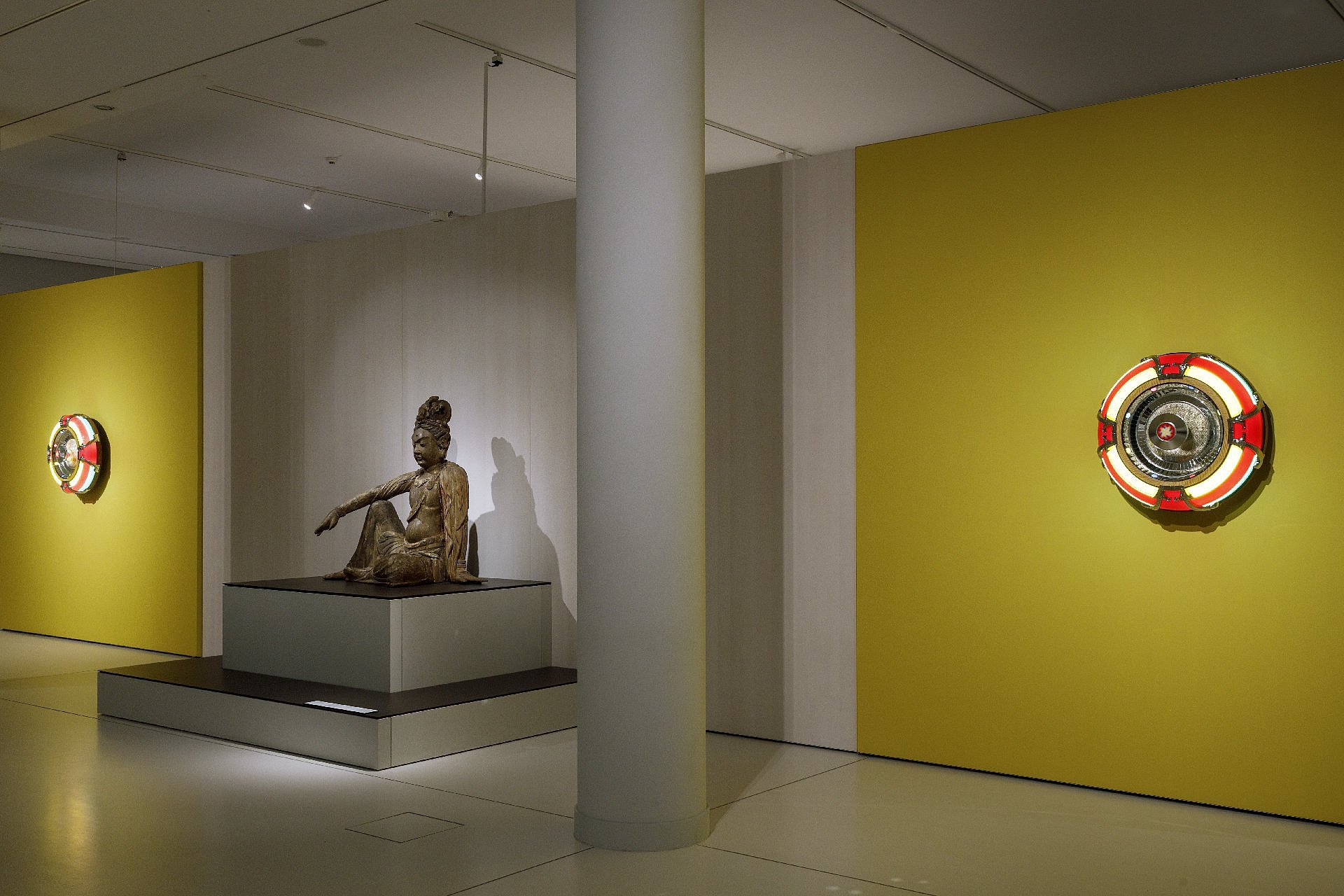 gelbe Wände mit seltsam-bunten Objekten auf ihnen, dazwischen eine Buddha-Statue