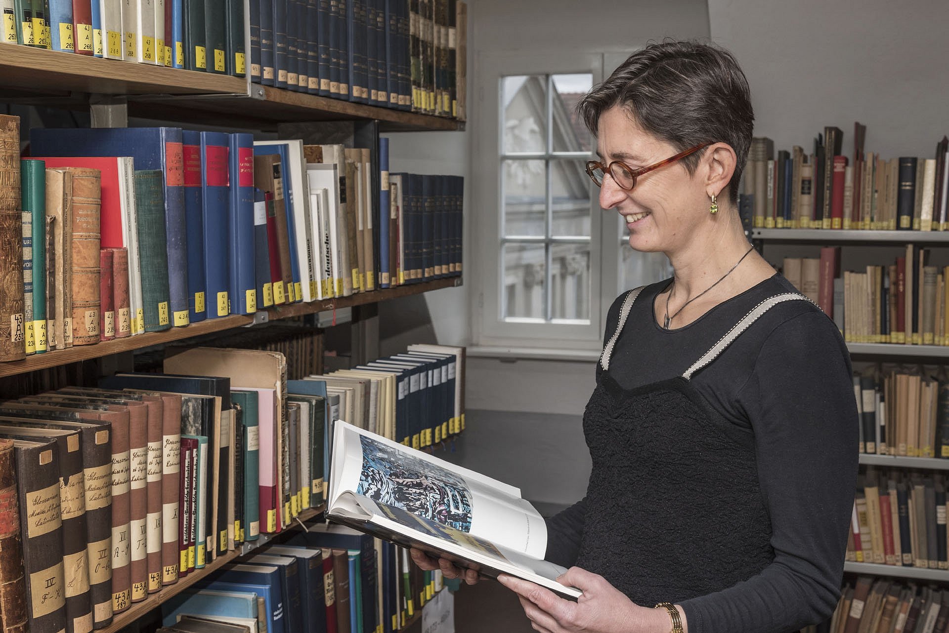 Frau steht lesend vor einem Bücherregal