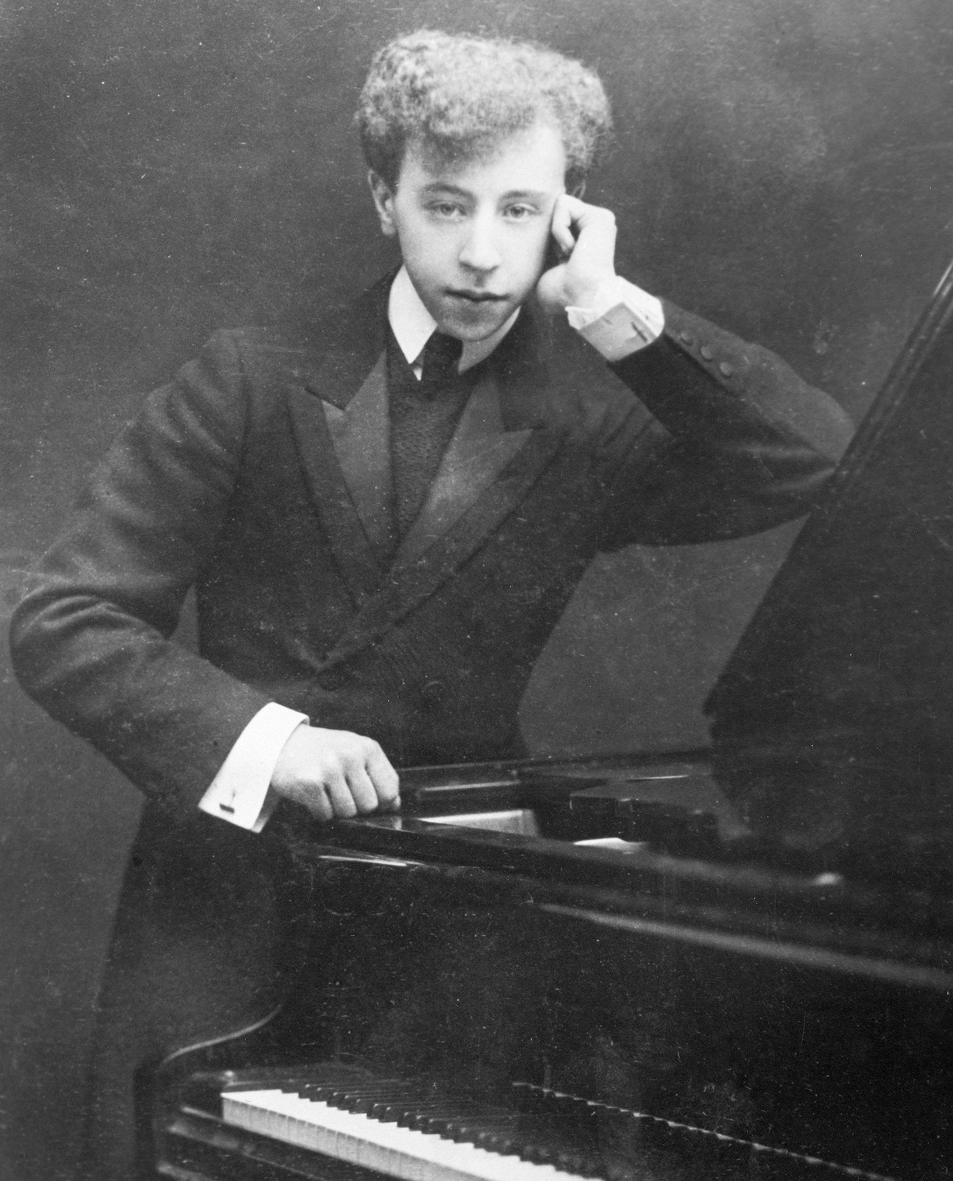 Historisches Porträt eines jungen Mannes im Anzug, stehend neben einem Klavier