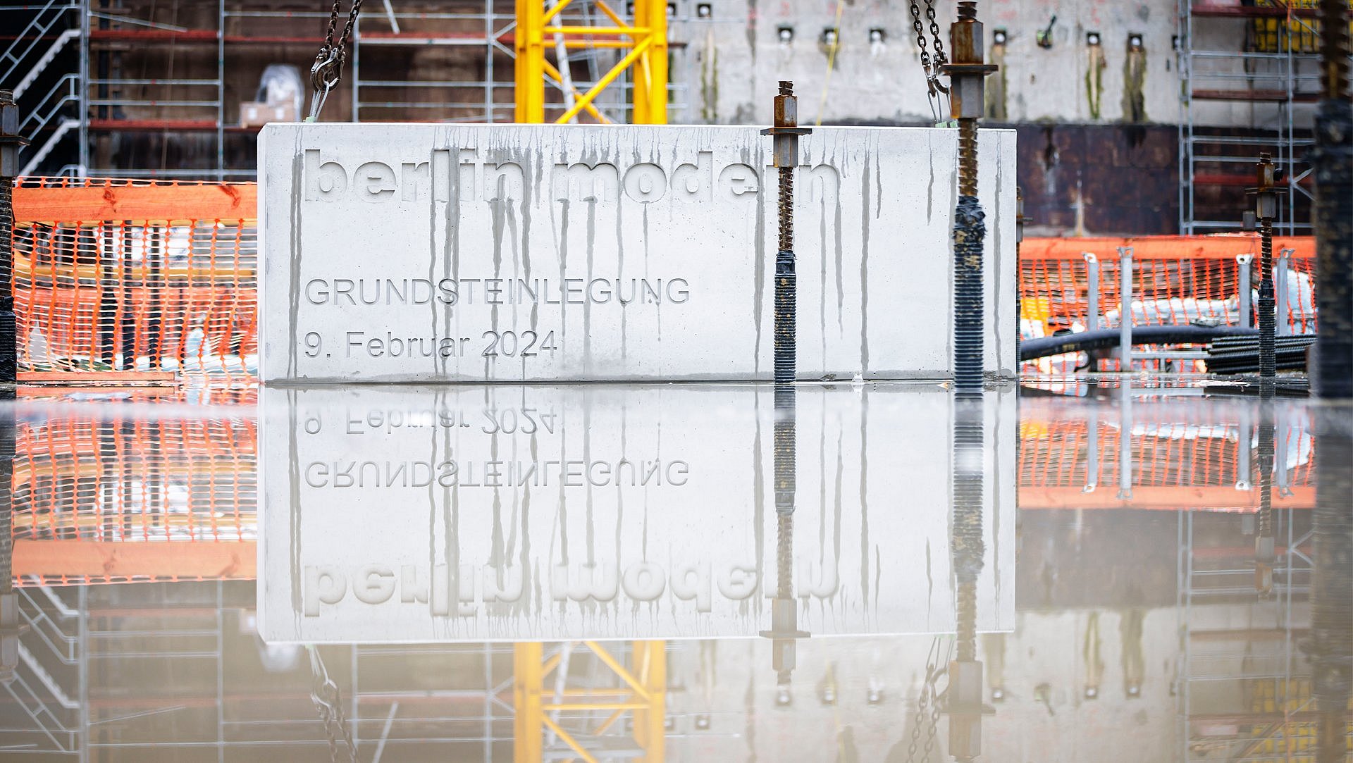 Ein rechteckiger Betonquuader spiegelt sich in der Pfütze am Grund einer Baugrube
