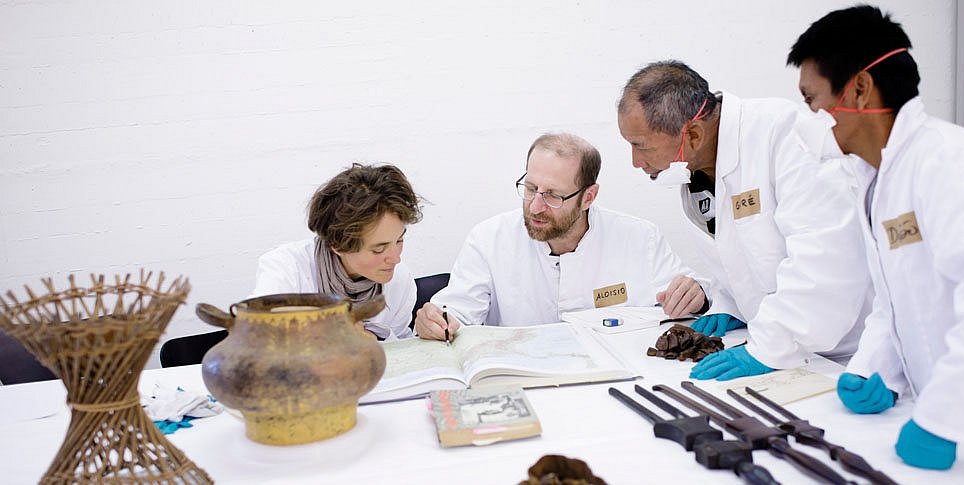 Vier Forscher*innen mit ethnologischen Objekten