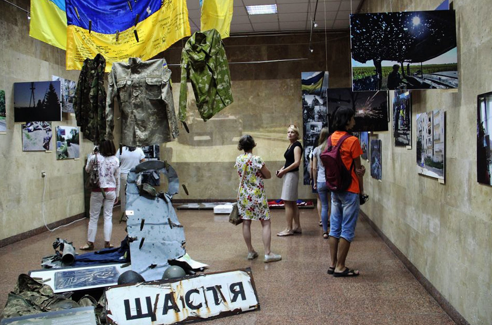 Menschen in einem Ausstellungsraum, von der Decke hängt eine ukrainische Fahne
