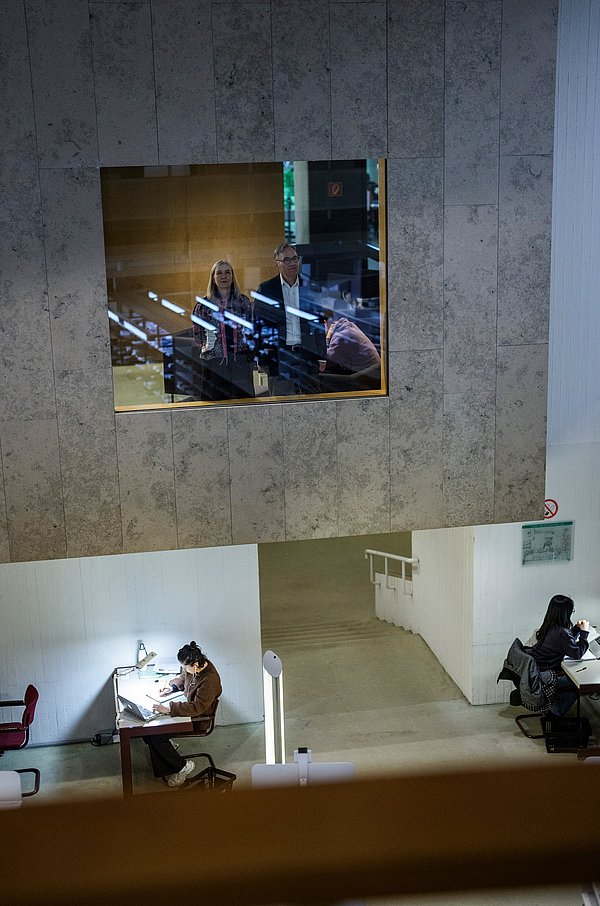 Zwei Menschen hinter einem Glasfenster in einer Bibliothek