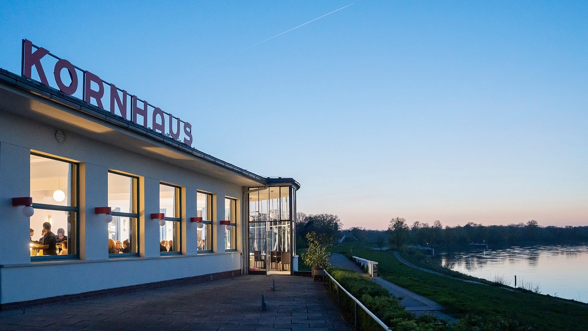 Moderner Bau mit Schriftzug "Kornhaus" im Sonnenuntergang neben großem Fluß