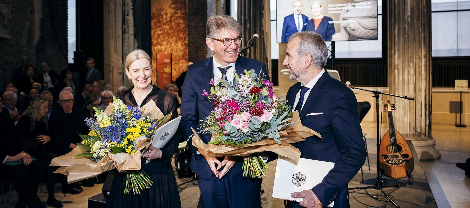 Kulturstaatsminister Wolfram Weimer (m.) überreichte Hermann Parzinger (r.) und Marion Ackermann (l.) neben einer Urkunde vom Bundespräsidenten und Kanzler auch einen Abschieds- bzw. Willkommensblumenstrauß. 