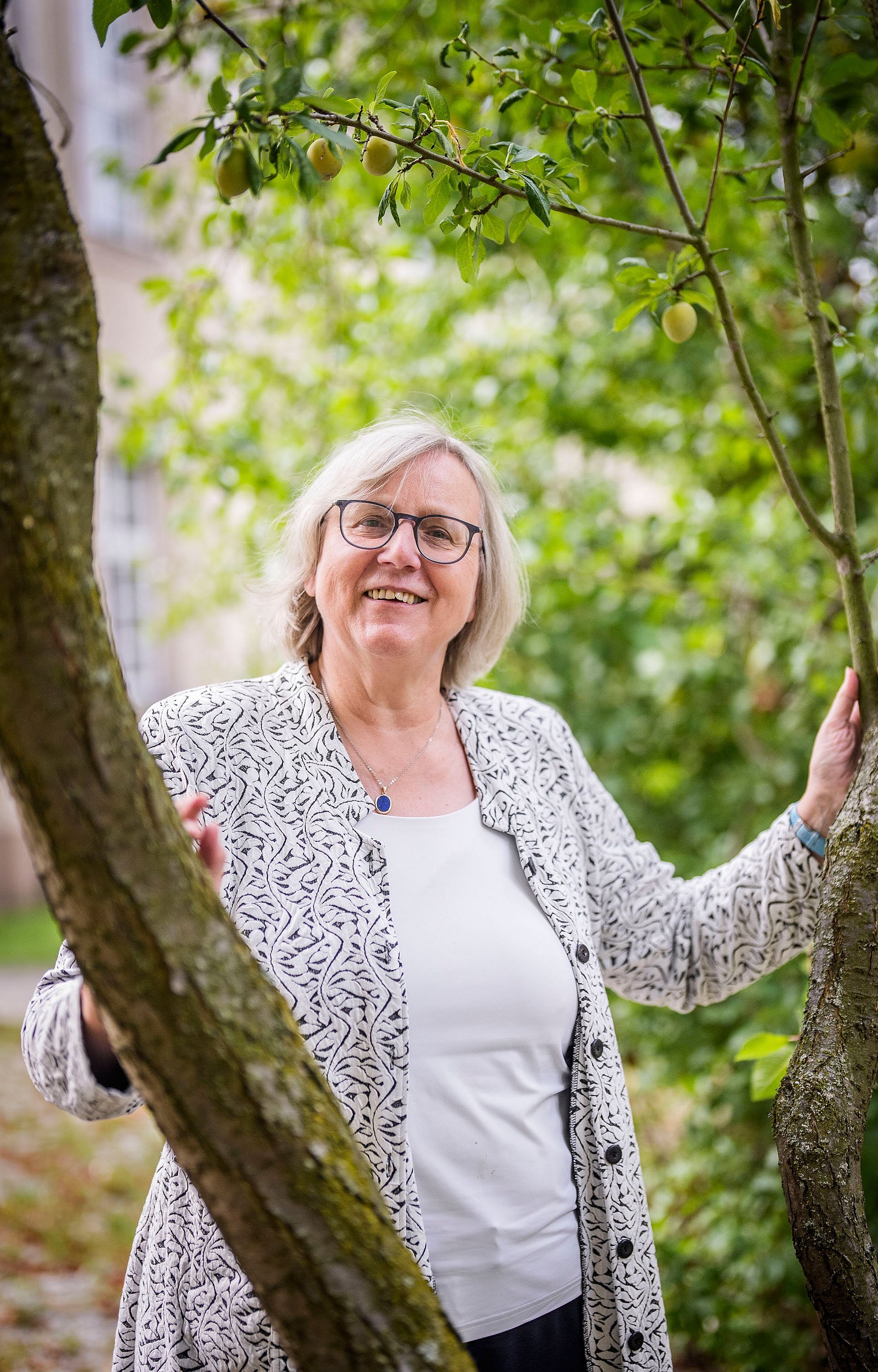 Frau steht zwischen einer Astgabel und stützt sich auf einem Stamm ab