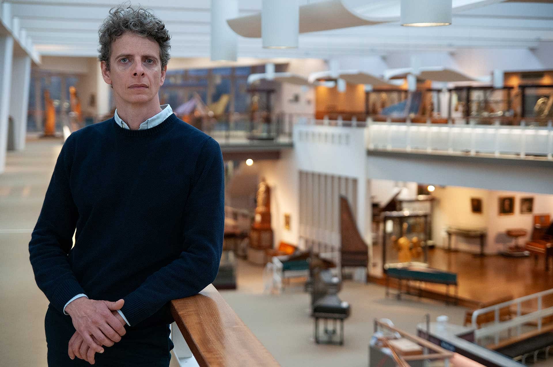 Mann steht am Geländer in einem offenen Museumsraum mit Instrumenten