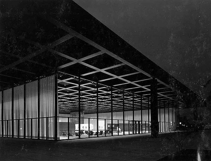 Schwarz-Weiß Fotografie mit Blick auf ein von innen beleuchtetes, modernes gläsernes Gebäude bei Nacht (öffnet Vergrößerung des Bildes)