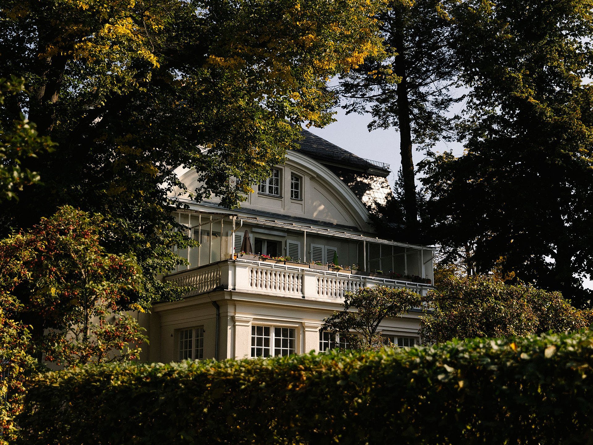 Blick auf eine Villa hinter Hecken und unter Bäumen