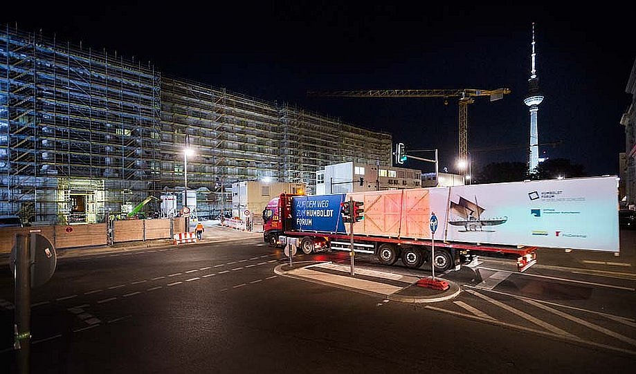 Vor der Kulisse des nächtlichen Berlins fährt ein mit einer großen Kiste beladener LKW eine Straße entlang (öffnet Vergrößerung des Bildes)