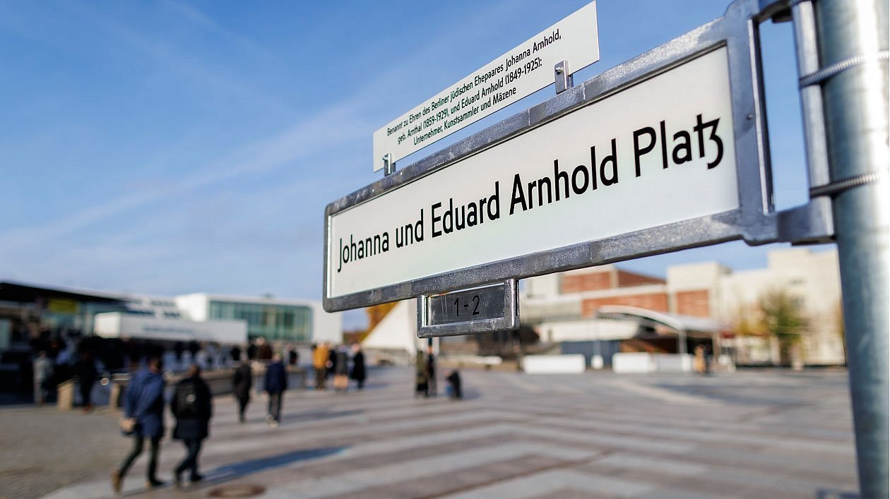 Neues Straßenschild vor belebtem Platz
