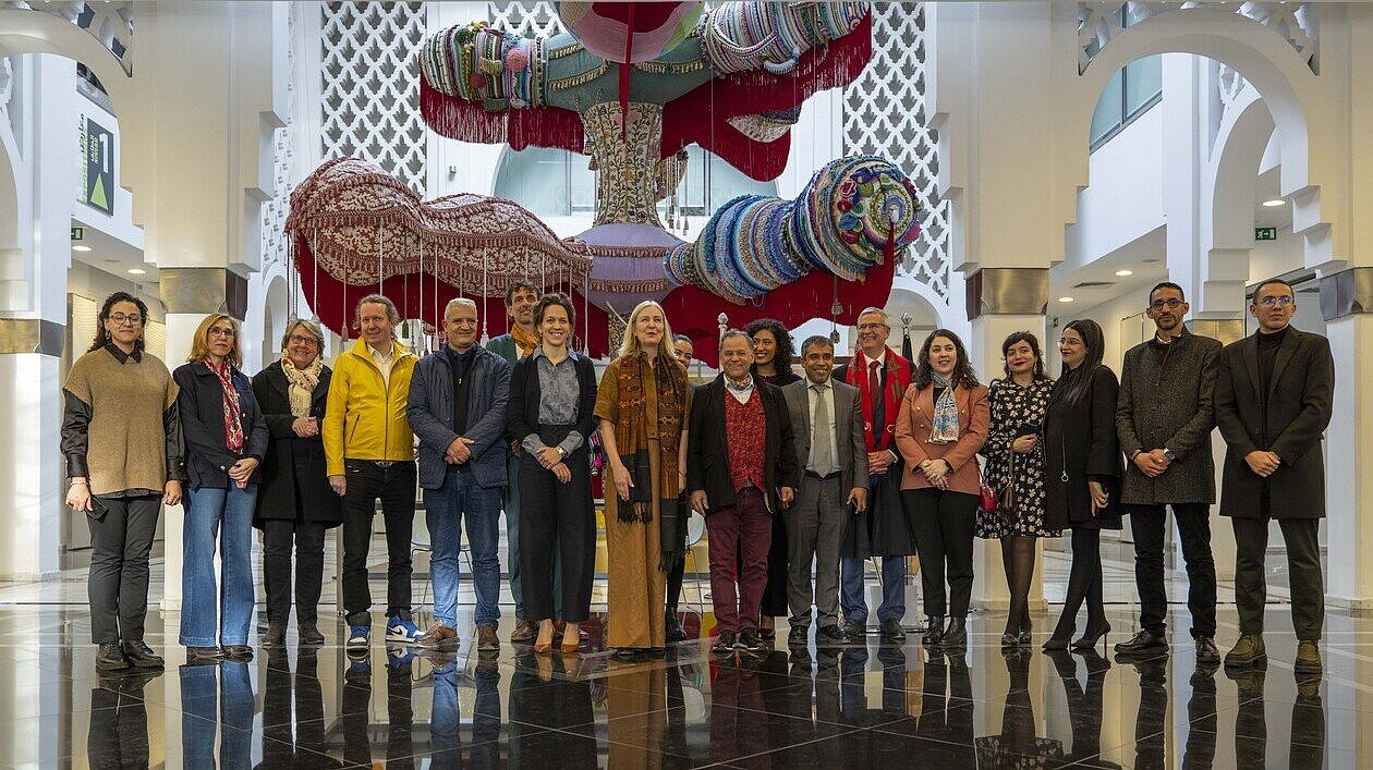 Mehrere Personen stehen für ein Gruppenfoto in einem Museumsgebäude in Rabat vor einer großen farbigen Installation.