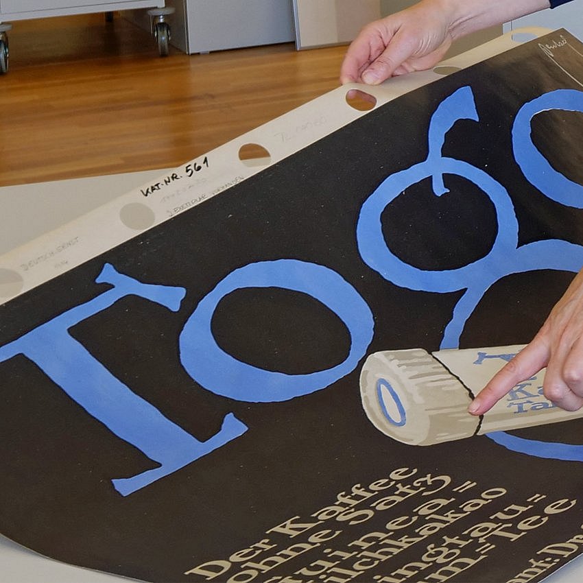 Ein Finger zeigt auf ein schwarzes Plakat mit Werbung für Kaffeetabletten