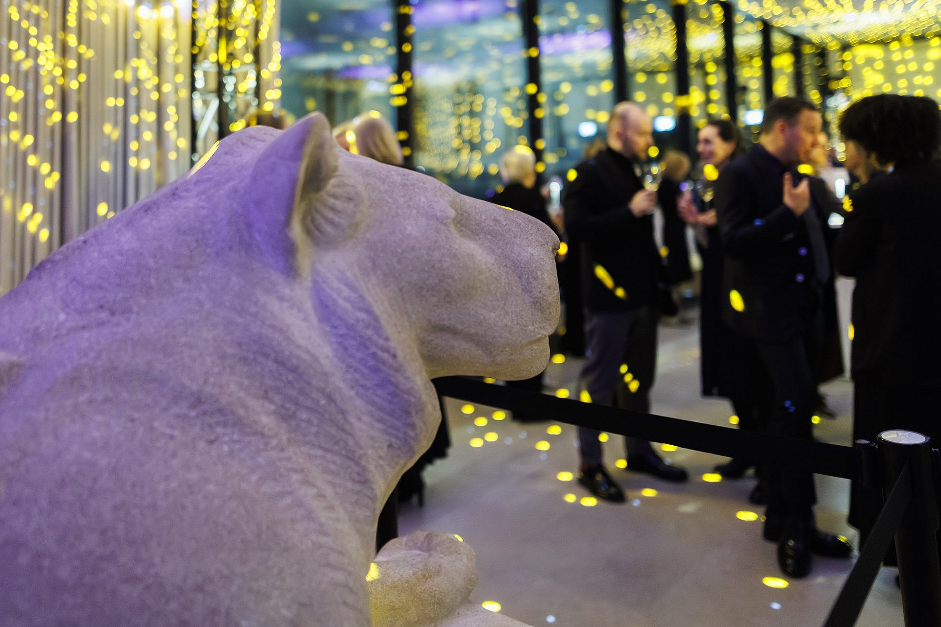 Skulptur eines liegenden Löwen im Foyer der James-Simon-Galerie; im Hintergrund Gäste beim Jahresempfang mit violetter und goldener Lichtprojektion.