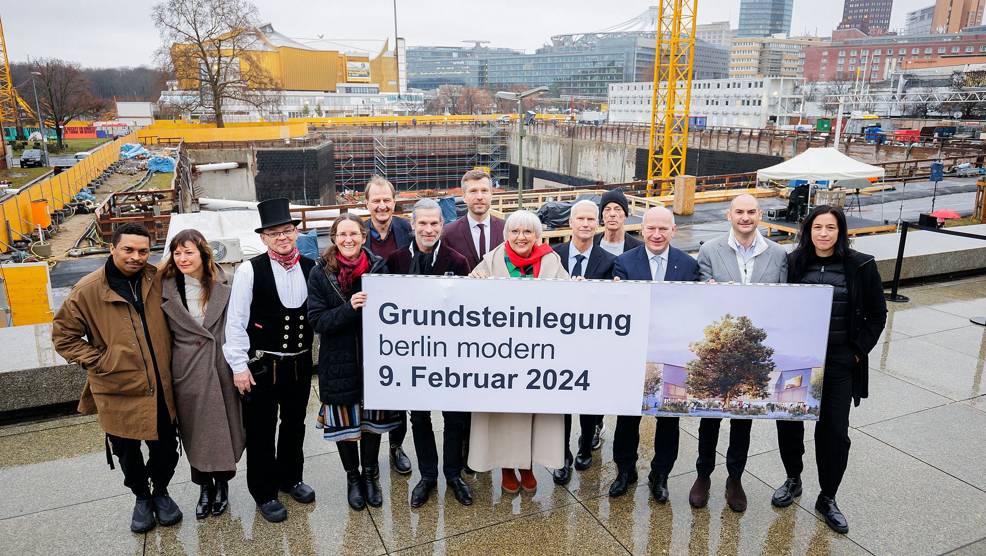 Eine Personengruppe posiert mit Schild vor einer Baugrube