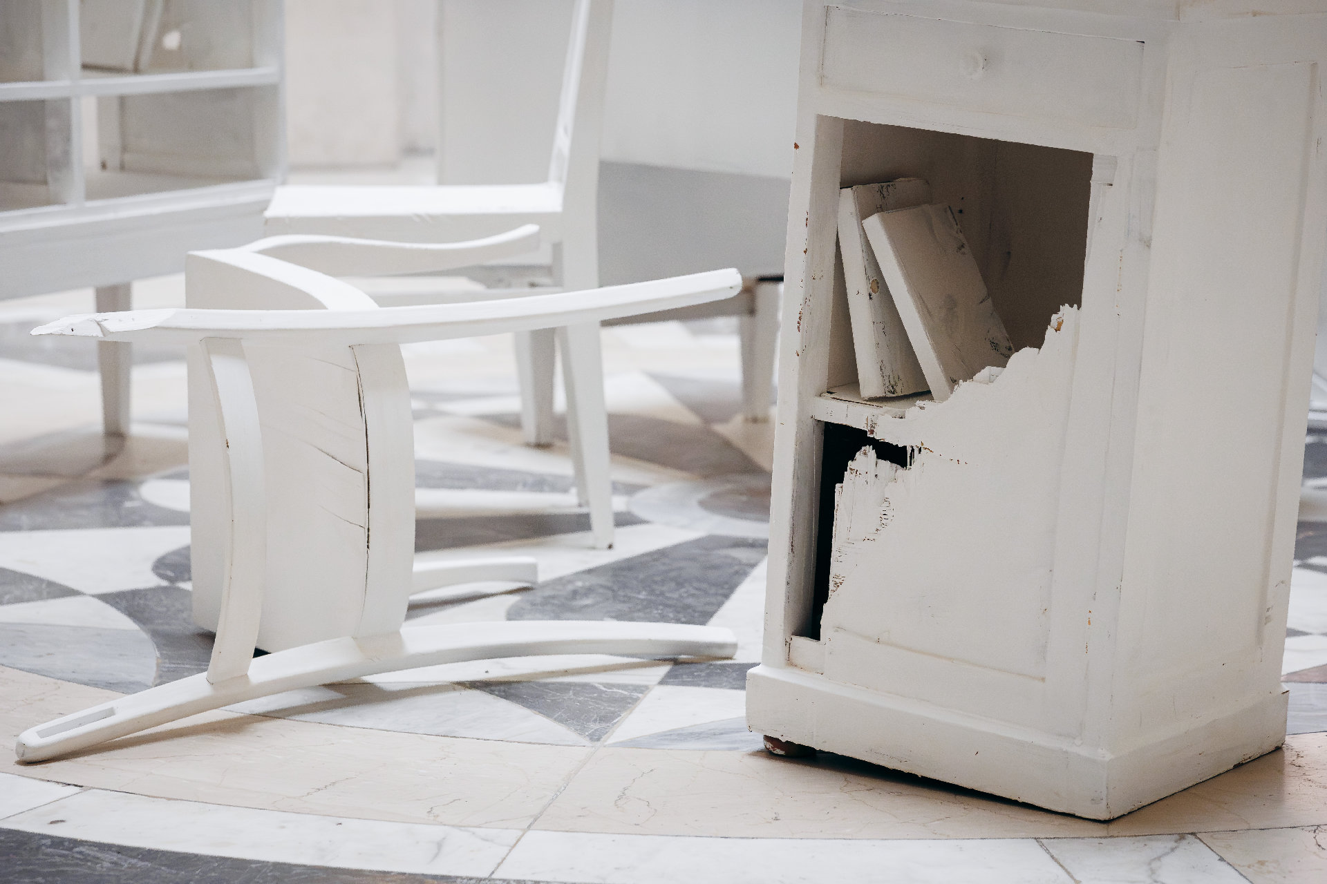 umgekippter weißer Stuhl neben kaputtem Schrank