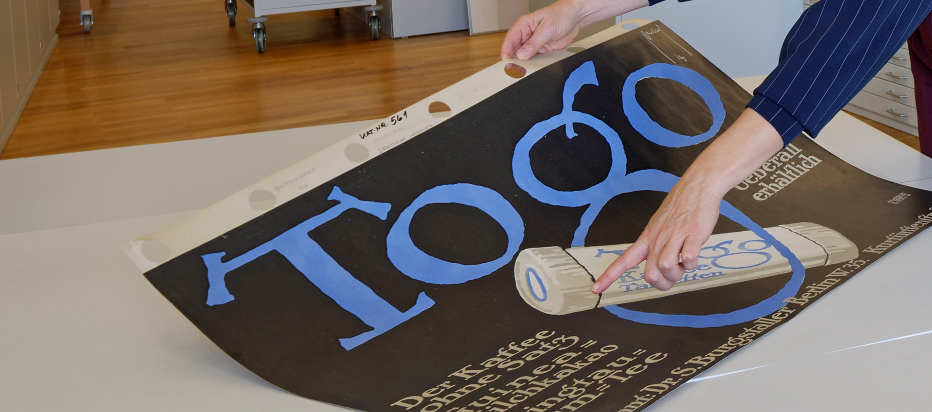 Ein Finger zeigt auf ein schwarzes Plakat mit Werbung für Kaffeetabletten